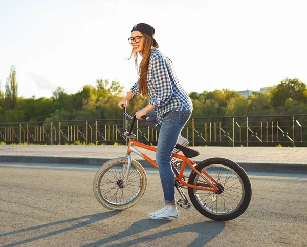 Adorável jovem mulher em um chapéu montando uma bicicleta no fundo da cidade — Fotografia de Stock