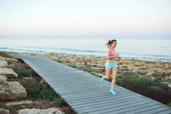 Νέα αθλητικά γυναίκα που τρέχει κατά μήκος ένα μονοπάτι δίπλα στη θάλασσα — Φωτογραφία Αρχείου