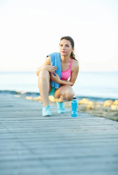 Sonniger Morgen am Strand, athletische Frau ruht sich nach dem Laufen aus — Stockfoto