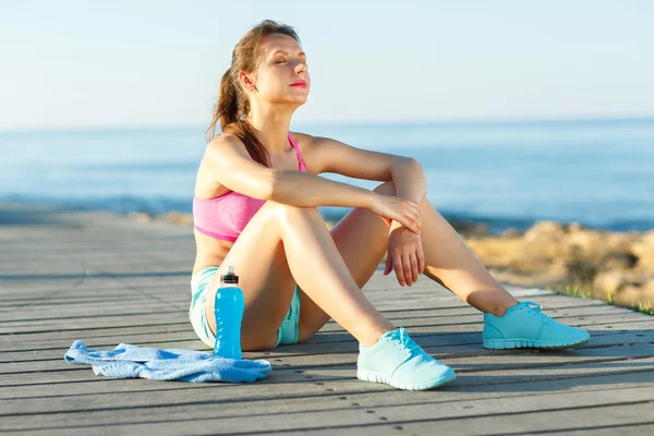 Sonniger Morgen am Strand, athletische Frau ruht sich nach dem Laufen aus — Stockfoto
