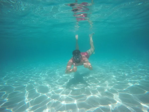 Человек в очках с большими пальцами вверх ныряя под водой — стоковое фото
