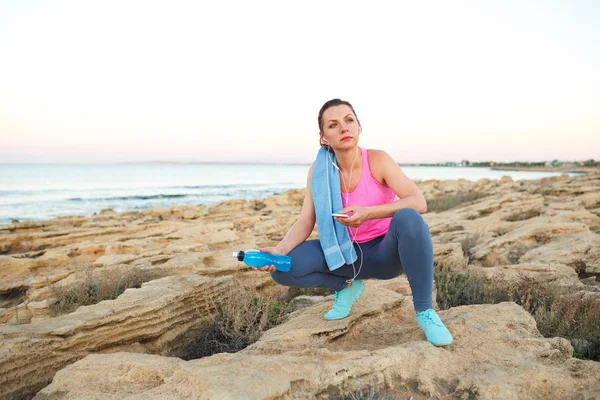 Frau sitzt nach dem Morgenlauf auf den Felsen am Meer — Stockfoto