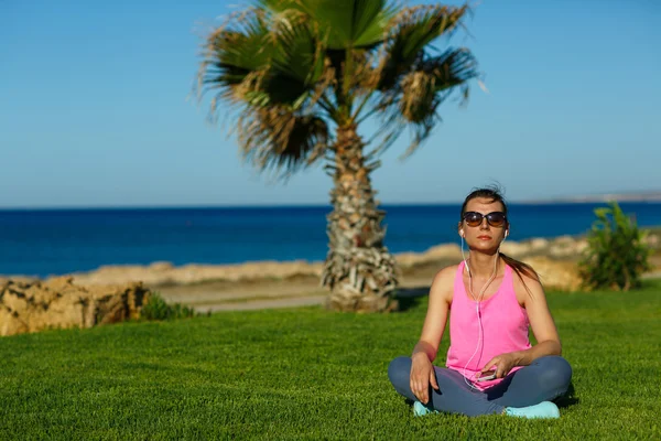 Спортивная девушка медитирует на траве у моря, практикует йогу — стоковое фото