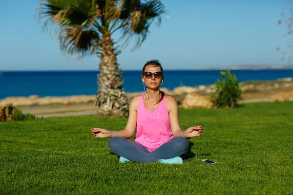 Deporte chica medita en la hierba cerca del mar, la práctica de yoga —  Fotos de Stock