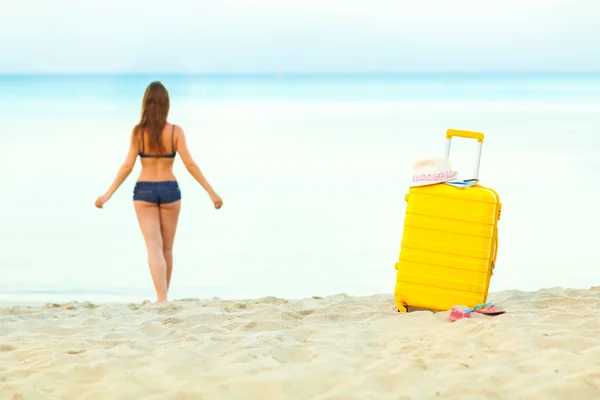 Maleta amarilla en la playa y una chica camina hacia el mar en th —  Fotos de Stock