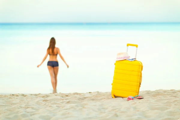 Yellow suitcase on the beach and a girl walks into the sea in th — Stock Photo, Image