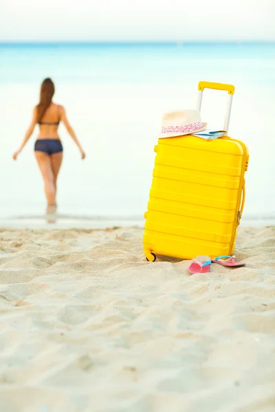 Maleta amarilla en la playa y una chica camina hacia el mar en th —  Fotos de Stock