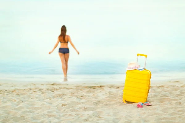 Gul resväska på stranden och en flicka går in i havet i th — Stockfoto