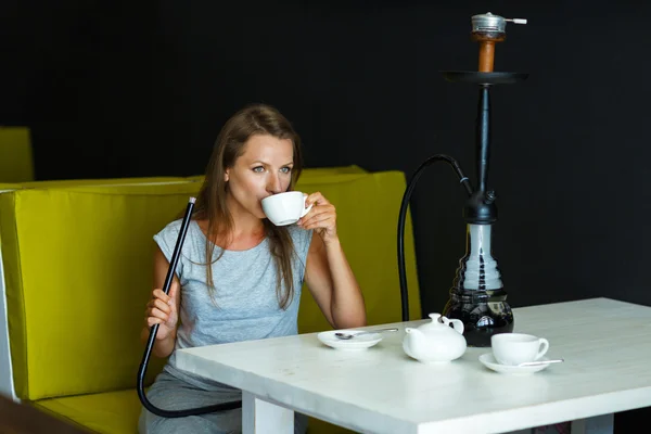 Mulher bonita fumando um narguilé e bebendo chá em um café — Fotografia de Stock