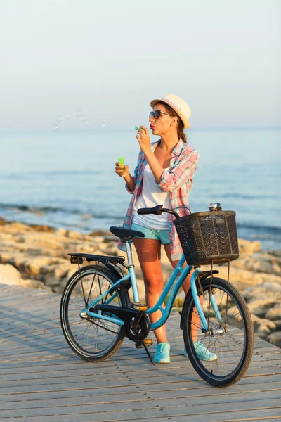 Ανέμελη γυναίκα με ποδήλατο στέκεται πάνω σε ένα ξύλινο μονοπάτι στη θάλασσα — Φωτογραφία Αρχείου