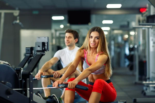 Atletik erkek ve kadının simülatörü cros içinde kürek üzerinde egzersiz yapması — Stok fotoğraf