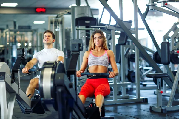 Atletik erkek ve kadının simülatörü cros içinde kürek üzerinde egzersiz yapması — Stok fotoğraf