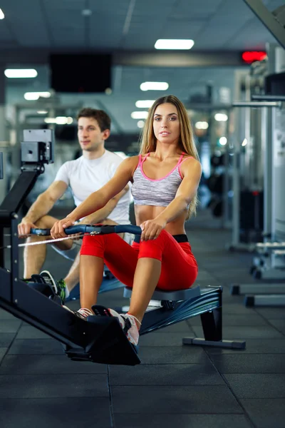 Atlético hombre y mujer haciendo ejercicio en simulador de remo en cros — Foto de Stock