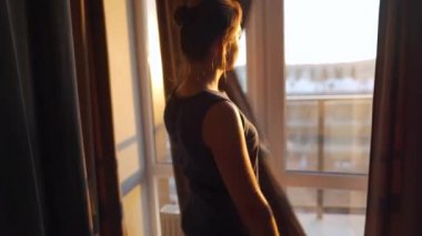 Kadın, güneş ışığını odaya almak için perdeleri açar.