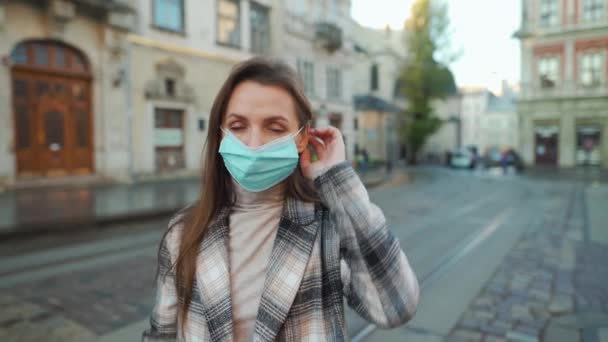 Pandemiskt skydd av Covid-19 coronavirus.Kvinna i rock står i mitten av torget, sätter på sig en skyddande medicinsk mask, sedan sätter på glasögon — Stockvideo