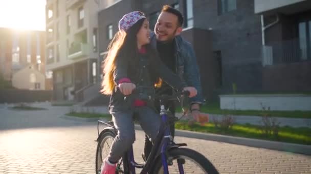 Pappa lär dottern cykla i solnedgången. Långsamma rörelser — Stockvideo