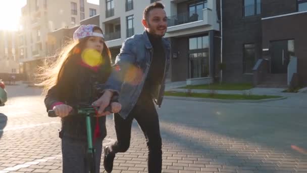 Dad is teaching daughter how to ride a scooter at sunset. Slow motion — Stock Video