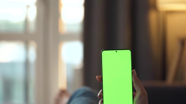 Frau zu Hause auf dem Sofa liegend und Smartphone mit grünem Bildschirm im vertikalen Modus. Mädchen surfen im Internet, schauen sich Inhalte, Videos, Blogs an. POV. — Stockvideo