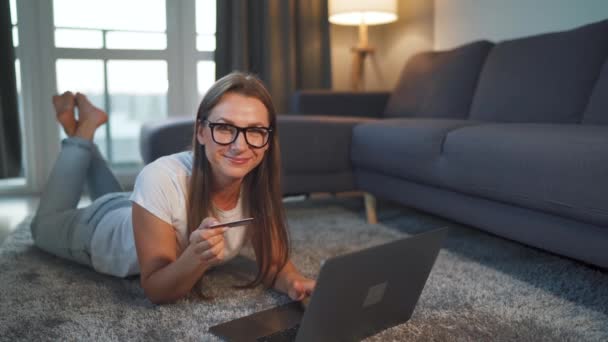 Mujer está tirada en el suelo y hace una compra en línea con una tarjeta de crédito y un ordenador portátil. Compras en línea, tecnología de estilo de vida — Vídeos de Stock