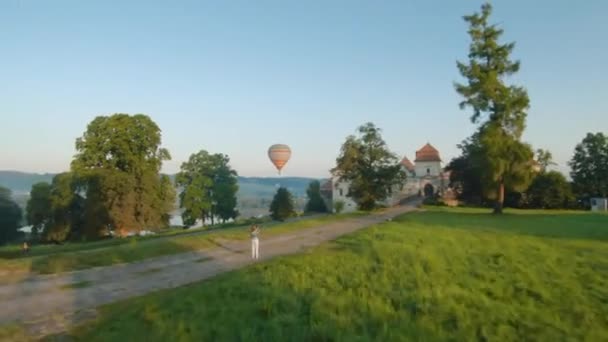 Bunte Heißluftballons fliegen im Morgennebel über die mittelalterliche Burg und den See. Frau macht Foto mit Smartphone und Luftballons — Stockvideo