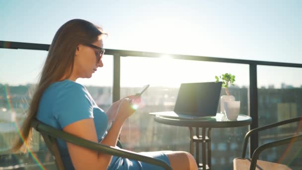 Γυναίκα που χρησιμοποιεί smartphone στο μπαλκόνι με φόντο το ηλιοβασίλεμα. Εξωτερικό γραφείο. Έννοια απομακρυσμένης εργασίας — Αρχείο Βίντεο