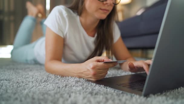 Frau mit Brille liegt auf dem Boden und kauft online mit Kreditkarte und Laptop ein. Online-Shopping, Lifestyletechnologie — Stockvideo