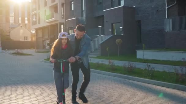 Papá le está enseñando a su hija a montar un scooter al atardecer. — Vídeos de Stock