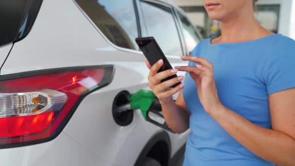 Mujer usando smartphone mientras su coche está repostando — Vídeos de Stock