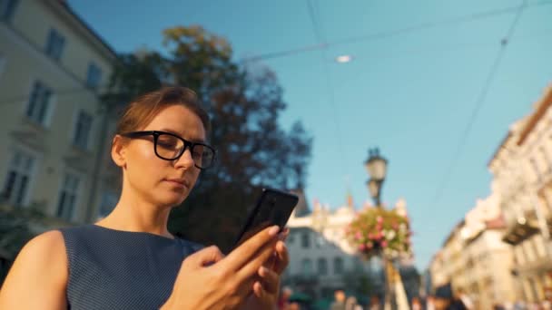 Mujer en gafas de pie en una calle vieja y usando un teléfono inteligente — Vídeo de stock