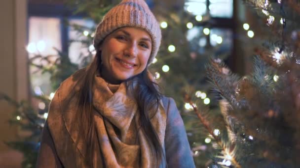 Portret van een gelukkige vrouw tegen de achtergrond van kerstversieringen. Ze wrijft over haar handen en houdt ze warm tegen de kou. — Stockvideo