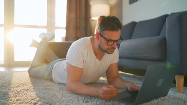 A szemüveges férfi a földön fekszik, és online vásárol hitelkártyával és laptoppal. Online vásárlás, életmód technológia