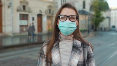 Covid-19 koronavirüsünün pandemik koruması. Ceketli, gözlüklü ve koruyucu sağlık maskeli bir kadın portresi. Meydanın ortasında duruyor..