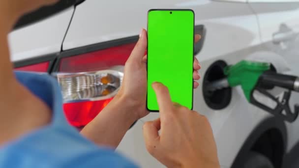 Жінка використовує мобільний додаток в смартфоні для оплати за дозаправку автомобіля. Смартфон із зеленим екраном. Клавіша Chroma — стокове відео