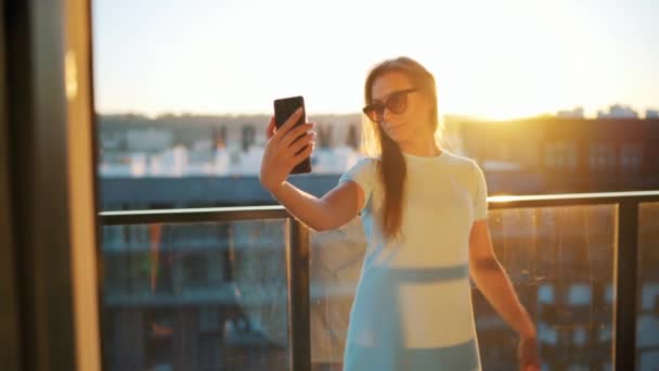 Mujer tomando selfie en el balcón al atardecer — Vídeo de stock