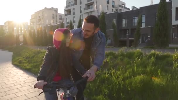 Papá le está enseñando a su hija a andar en bicicleta al atardecer. Movimiento lento — Vídeos de Stock