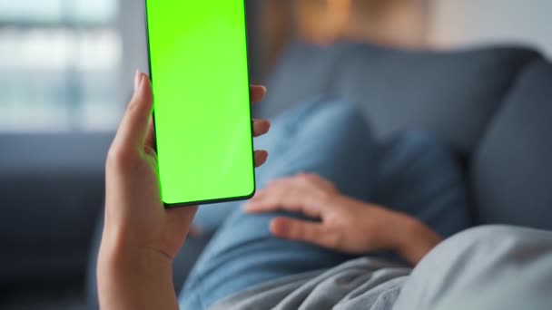 Frau zu Hause auf dem Sofa liegend und Smartphone mit grünem Bildschirm im vertikalen Modus. Mädchen surfen im Internet, schauen sich Inhalte, Videos, Blogs an. POV. — Stockvideo