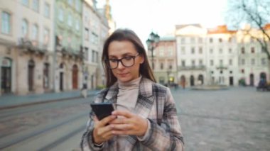 Eski bir caddede yürüyen, akıllı telefon kullanan ve fotoğraf çeken bir kadın.