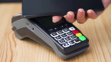 Akıllı telefondan yapılan temassız ödeme. Kablosuz ödeme konsepti. Yakın plan, kadın banka terminalindeki siparişi ödemek için akıllı telefon nakitsiz cüzdan teknolojisi kullanıyor..