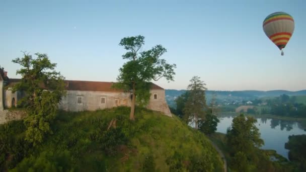 La montgolfière colorée survole le château médiéval et le lac dans le brouillard matinal. Vol manœuvrable. Voyage, aventure, festival. — Video