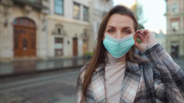 Pandemiskt skydd av Covid-19-koronavirus. Kvinna i rock står i mitten av torget, sätter på sig en skyddande medicinsk mask — Stockvideo