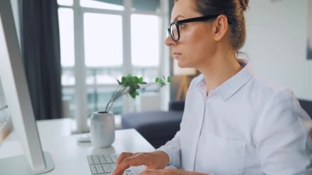 Donna con gli occhiali che digita su una tastiera del computer. Concetto di lavoro a distanza. — Video Stock