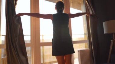 Kadın, güneş ışığını odaya almak için perdeleri açar.
