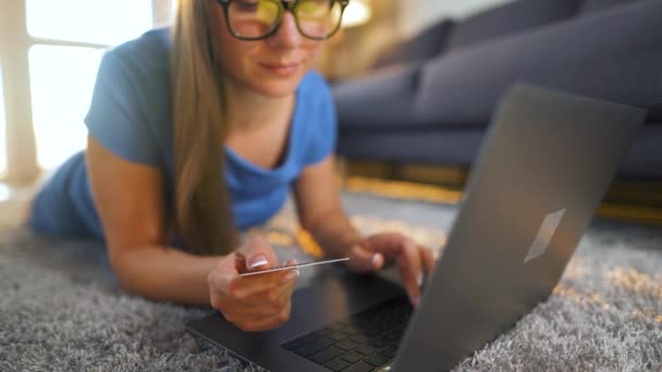 Frau mit Brille liegt auf dem Boden und kauft online mit Kreditkarte und Laptop ein. Online-Shopping, Lifestyletechnologie — Stockvideo