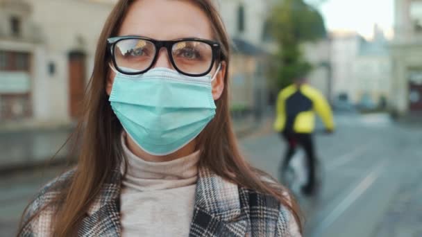 Pandemická ochrana koronaviru Covid-19. Portrét ženy v kabátě, brýlích a ochranné lékařské masce. Ona stojí uprostřed náměstí.. — Stock video