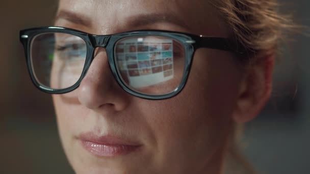 戴眼镜的女人看着监视器和上网。显示器屏幕反映在眼镜上.晚上工作。内政部。远程工作 — 图库视频影像