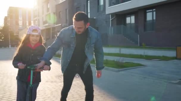 Dad is teaching daughter how to ride a scooter at sunset — Stock Video