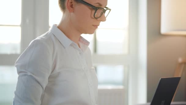 Mujer con gafas está sentado en el sofá en una habitación acogedora y trabajando en un ordenador portátil. Concepto de trabajo remoto. — Vídeos de Stock