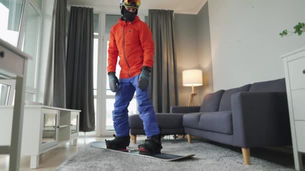 Fajny film. Człowiek przebrany za snowboardzistę jeździ na snowboardzie po dywanie w przytulnym pokoju. Czekam na śnieżną zimę. — Wideo stockowe