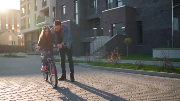 Papá le está enseñando a su hija a andar en bicicleta al atardecer. — Vídeos de Stock