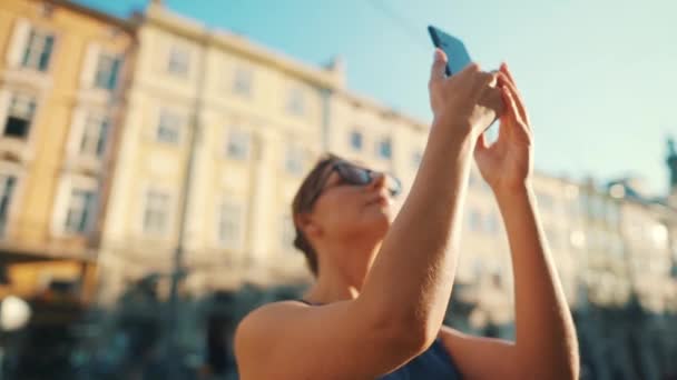 Femme se tient dans une vieille rue et prend une photo ou une vidéo sur un smartphone au coucher du soleil. Mouvement lent — Video